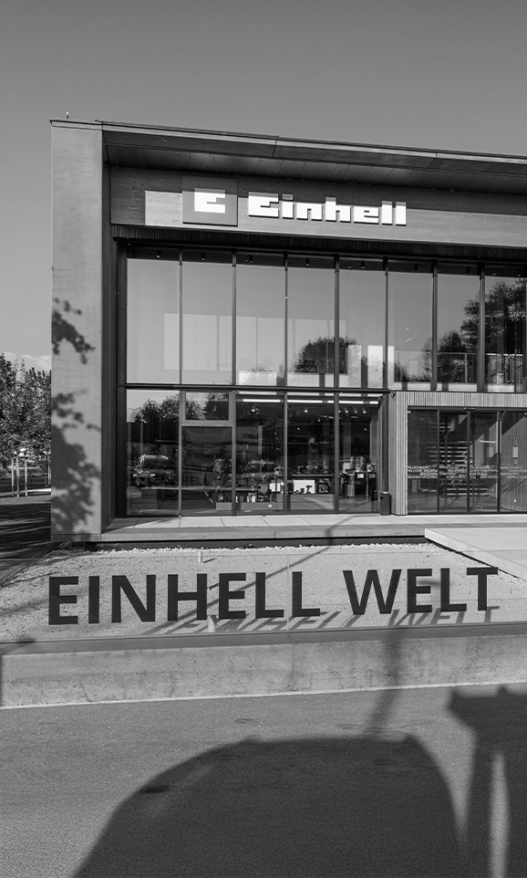 Imagen en blanco y negro del mundo de Einhell: edificio moderno de empresa con el logo de Einhell y un gran grupo de empleados.