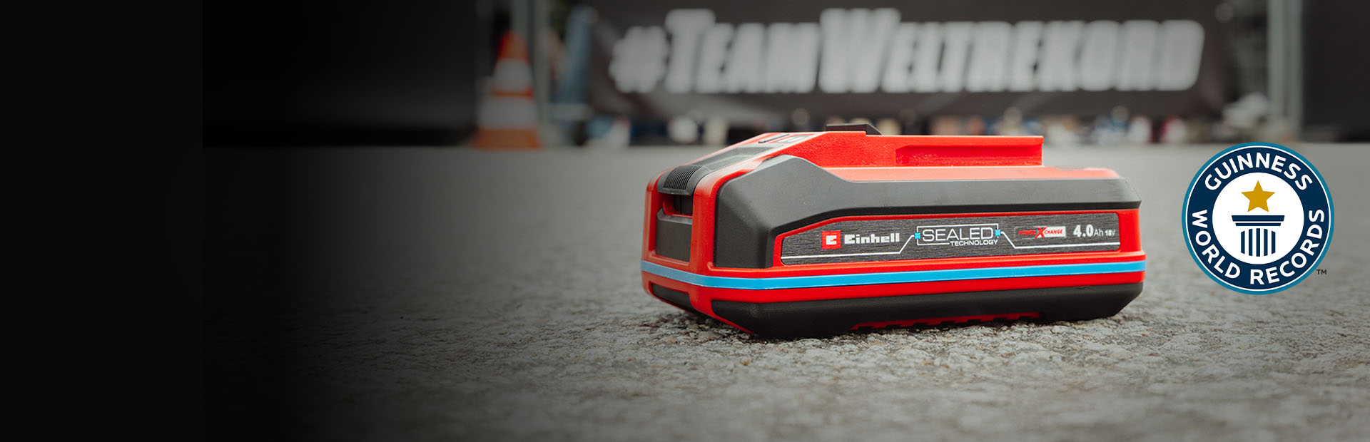 Una batería Einhell SEALED Power X-Change de 4.0 Ah yace sobre asfalto, con el logo de "Record Holder" de Guinness World Records a la derecha.