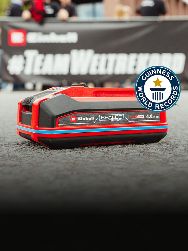 Una batería Einhell SEALED Power X-Change de 4.0 Ah yace sobre asfalto, con el logo de "Record Holder" de Guinness World Records a la derecha.