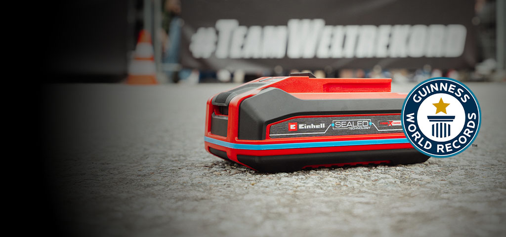 Una batería Einhell SEALED Power X-Change de 4.0 Ah yace sobre asfalto, con el logo de "Record Holder" de Guinness World Records a la derecha.