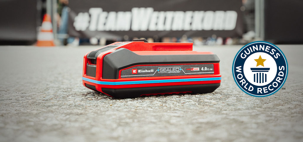 Una batería Einhell SEALED Power X-Change de 4.0 Ah yace sobre asfalto, con el logo de "Record Holder" de Guinness World Records a la derecha.